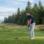 A male golfer on a Washington State tee box addressing a ball with a distance driver.